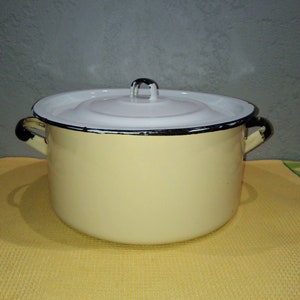 Könnte beinhalten: Ein weißer Emailletopf mit schwarzem Rand und schwarzen Griffen. Der Topf hat einen weißen Deckel mit einem schwarzen Knopf.