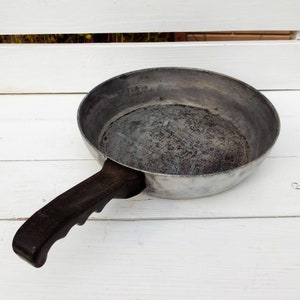 May include: A silver frying pan with a black handle. The pan has a worn, used appearance.
