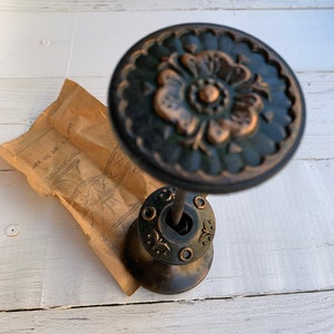 Peut inclure: Un crochet vintage en métal orné, avec une finition verte et cuivre. Le crochet présente un motif floral décoratif et une base ronde. Le crochet est attaché à un paquet en papier brun.
