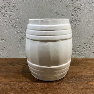May include: White ceramic barrel-shaped vase with a textured surface.