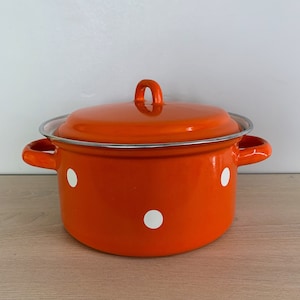 May include: Orange enamel pot with white polka dots and a silver rim. The pot has two handles and a lid.