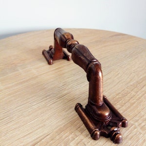 May include: A close-up of a brown metal handle with intricate details. The handle is mounted on a light wood surface.