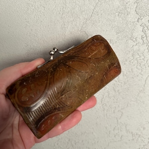 May include: A rectangular brown leather coin purse with a floral pattern and a silver clasp. The purse is held in a hand and has a vintage aesthetic.