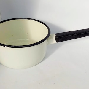 Peut inclure: Une casserole en émail blanc avec une poignée noire. La casserole a un bord noir autour du haut.