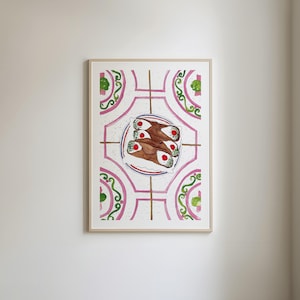 May include: Watercolor print of cannoli pastries on a decorative plate. The plate sits on a white background with pink and green floral patterns. The artwork is framed in a light wood frame.