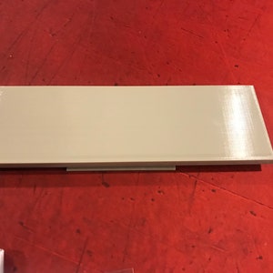 Op de afbeelding: Een lichtbeige rechthoekige plank met een glad, licht getextureerd oppervlak. De plank is gemaakt van plastic en heeft een eenvoudig, modern ontwerp.