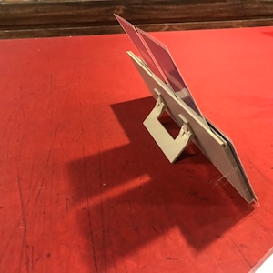 Op de afbeelding: Een witte plastic kaarthouder met twee sleuven voor kaarten. De houder is schuin geplaatst om de kaarten te tonen. De houder staat op een rood oppervlak.