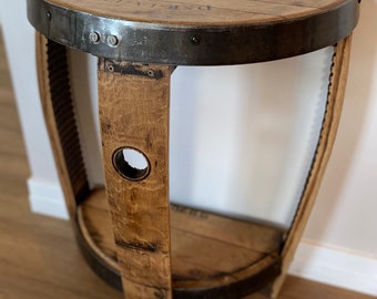 May include: A half-round wooden table made from a repurposed barrel with a metal band and a shelf. The top of the table has the text "CEDAR BROOK" printed on it.