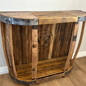 May include: A rustic wooden console table made from reclaimed wood barrels. The table has a curved top and a shelf. The wood is a natural brown color with a distressed finish. The table has metal accents on the top and bottom.
