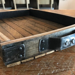 May include: A wooden tray with a black metal handle and metal accents. The tray is made from reclaimed wood and has a rustic look.