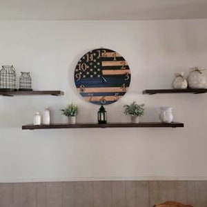 May include: Three wooden shelves with decorative items on them, including a clock with an American flag design, a lantern, and two vases. The clock has black and brown stripes with a white star pattern.