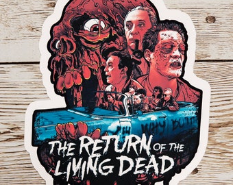 May include: A sticker featuring a colorful illustration of characters from the movie "The Return of the Living Dead". The sticker features a zombie with a red, orange, and yellow face, and a blue car with people inside. The text "The Return of the Living Dead" is written in black and white.