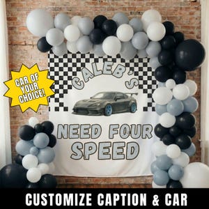 May include: A car-themed party backdrop with a banner featuring a gray sports car and the text "Caleb's Need Four Speed." The backdrop is framed by a balloon arch in black, white, and gray. A yellow starburst reads "Car of Your Choice!"