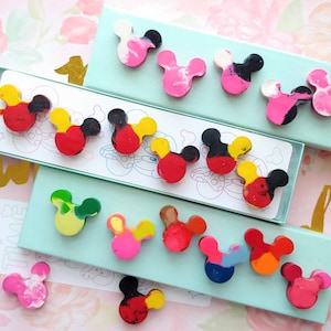 May include: A set of colorful Mickey Mouse shaped crayons in various colors, including red, yellow, blue, green, and pink. The crayons are arranged in a box with a blue background and the text "Reading Time" on a white tag.