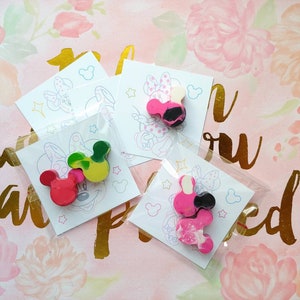 May include: Four small bags with white cardstock inside, each featuring a black and white line drawing of a cartoon mouse with large ears. Each bag contains a set of three small, colorful, hand-painted, wax crayons shaped like the cartoon mouse.