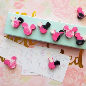 May include: A set of six pink, black, and white Mickey Mouse shaped crayons in a teal box. The crayons are arranged in a row on the box. There is a bookmark with the text "Reading Time" and four coloring pages with Mickey Mouse illustrations.