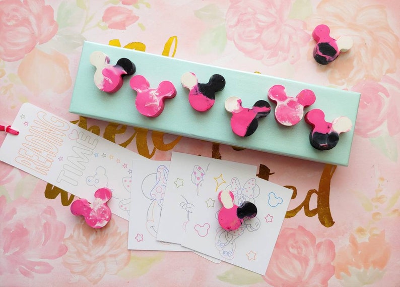 May include: A set of six pink, black, and white Mickey Mouse shaped crayons in a teal box. The crayons are arranged in a row on the box. There is a bookmark with the text "Reading Time" and four coloring pages with Mickey Mouse illustrations.