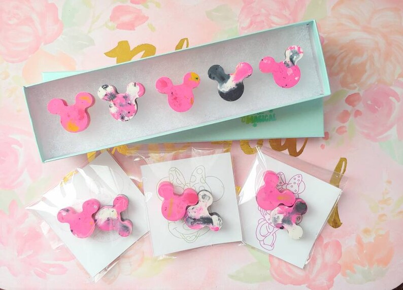 May include: A set of six pink and black resin Mickey Mouse head pins. The pins are packaged in a light blue box with the word "remarkable" printed on it. The pins are also packaged individually in clear plastic bags with white cards.