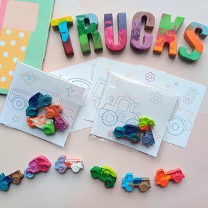 May include: A set of colorful crayon trucks and cars with coloring pages featuring trucks and cars. The crayons are arranged to spell the word "TRUCKS".