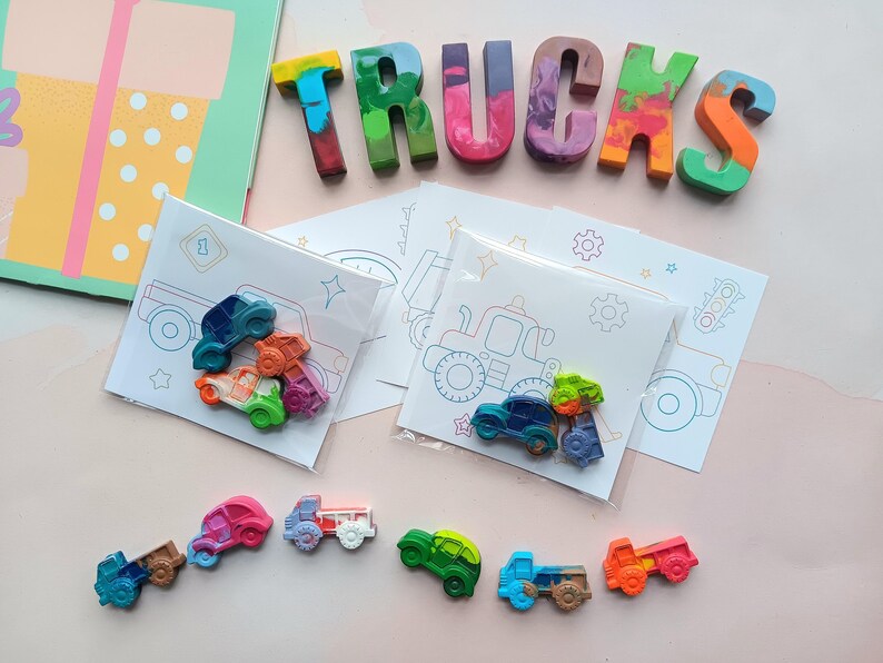 May include: A set of colorful crayon trucks and cars with coloring pages featuring trucks and cars. The crayons are arranged to spell the word "TRUCKS".