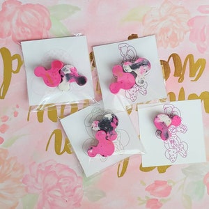 May include: Four pink and black Mickey Mouse head shaped resin ornaments on white cards with a black outline of Mickey Mouse.