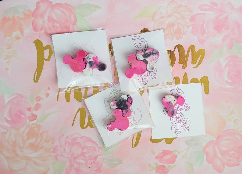 May include: Four pink and black Mickey Mouse head shaped resin ornaments on white cards with a black outline of Mickey Mouse.