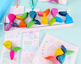 May include: A collection of multi-colored mermaid tail-shaped crayons paired with white paper bookmarks. The bookmarks feature line art of mermaids and sea life with the text "BOOKS ARE GREAT" and "ARE FUN" printed in colorful outlines.