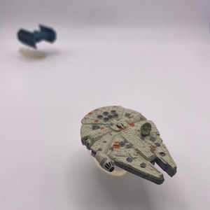 May include: A gray and white toy spaceship with orange and black details. The spaceship is a model of the Millennium Falcon from Star Wars.
