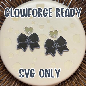 May include: Two black bow earrings with silver jump rings and clear heart charms. The earrings are on a white background with the text "Glowforge Ready" and "SVG Only".