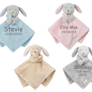 May include: Four personalized baby blankets with a plush grey dog attached. The blankets are blue, pink, beige, and grey. The blankets are embroidered with names and dates.