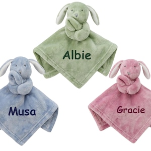May include: Three plush bunny security blankets in different colors. The green blanket has the name "Albie" embroidered on it. The blue blanket has the name "Musa" embroidered on it. The pink blanket has the name "Gracie" embroidered on it.