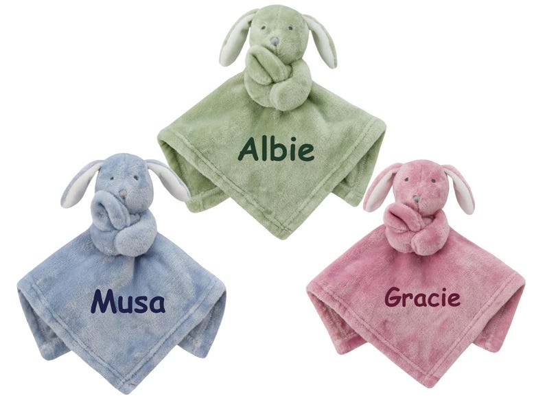 May include: Three plush bunny security blankets in different colors. The green blanket has the name "Albie" embroidered on it. The blue blanket has the name "Musa" embroidered on it. The pink blanket has the name "Gracie" embroidered on it.