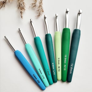 Könnte beinhalten: Sechs Häkelnadeln mit silbernen Spitzen und farbigen Griffen in Blau- und Grüntönen. Größen: 5.0mm-H/8, 6.0mm-J/10, 7.0mm, 8.0mm-L/11, 9.0mm-M/13, 10.0mm-N/15, und 12.0mm. Ideal zum Häkeln.