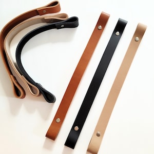Könnte beinhalten: Vier Lederriemen mit Metallbeschlägen. Die Riemen sind in verschiedenen Farben, darunter Braun, Schwarz und Beige.