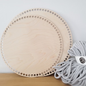 Könnte beinhalten: Zwei runde Holz-Strickrahmen mit Löchern am Rand, einer etwas kleiner als der andere. Eine Kugel grauen Garns befindet sich im Vordergrund mit einem weißen Etikett, auf dem "Bobbiny" steht.