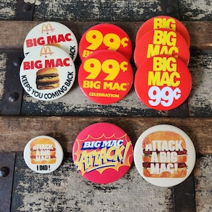 Peut inclure: Une collection de badges promotionnels Big Mac vintage. Les badges sont rouges, jaunes et blancs avec divers slogans et images Big Mac. Les badges comportent le texte "Big Mac", "99 cents", "Big Mac Celebration", "Attaquez un Big Mac" et "J'ai fait !"