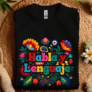 May include: A black crewneck sweatshirt featuring a colorful floral design surrounding the text "Habla y Lenguaje" in bold, multi-colored letters. The graphic includes various stylized flowers and leaves in shades of red, yellow, blue, and green.