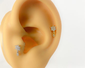 Könnte beinhalten: Ein Paar goldene Ohrstecker mit Blumenmuster und einem baumelnden Kristall. Die Ohrstecker sind im Ohr eines Modells zu sehen.