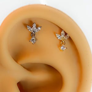 Könnte beinhalten: Zwei Ohrknorpel-Ohrringe in Gold und Silber mit Blumenmuster und einem baumelnden Kristall.