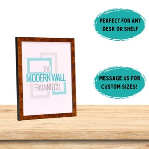 Op de afbeelding: Een bruin houten fotolijst met een zwarte rand. De lijst heeft een witte passe-partout en een wit label met de tekst "THE MODERN WALL FRAMING CO."