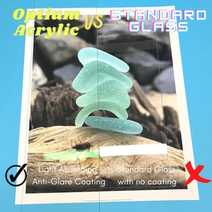May include: A side-by-side comparison of two pieces of glass, one with an anti-glare coating and one without. The glass with the anti-glare coating is labeled "Optium Acrylic" and the glass without the coating is labeled "Standard Glass". Both pieces of glass are clear and have a smooth surface. A stack of sea glass is placed on top of each piece of glass.