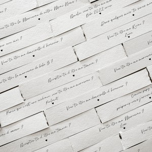 May include: White paper strips with black text asking "Will you be my..." followed by a role in a wedding party, such as "maid of honour", "matron of honour", "bridesmaid", or "godmother".