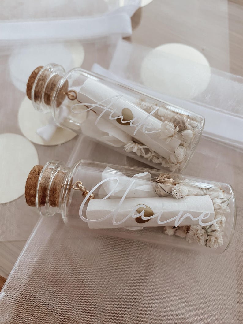 May include: Two glass bottles with cork stoppers filled with dried white flowers and a rolled up piece of paper with the names "Anne" and "Claire" written on them.