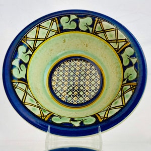 May include: A blue and green ceramic bowl with a geometric design. The bowl has a white center with a blue and yellow geometric pattern.