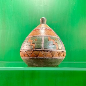 May include: A small, round, ceramic vase with a geometric pattern in shades of brown, green, and orange. The vase has a narrow neck and a wide base.