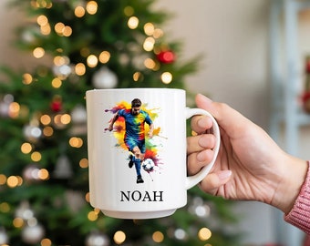 May include: White ceramic mug with a colorful illustration of a soccer player dribbling the ball. The mug has the name "NOAH" printed on the bottom.
