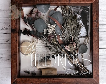 May include: A shadow box with a dark wood frame, showcasing a dried flower bouquet, eucalyptus leaves, and a pocket watch. The display includes a wedding invitation and wine corks. The text "HEDRICKS" and "10.30.2009" are visible.