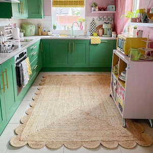 K&ouml;nnte beinhalten: Eine gr&uuml;ne K&uuml;che mit einem hellbraunen Jute-Teppich mit gewelltem Rand. Der Teppich liegt vor gr&uuml;nen Schr&auml;nken mit goldenen Griffen. Rechts im Bild befindet sich ein rosa Schrank mit einem gelben und schwarzen Regal.