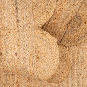 K&ouml;nnte beinhalten: Nahaufnahme eines nat&uuml;rlichen gewebten Teppichs aus Jutefasern. Der Teppich hat eine strukturierte, raue Oberfl&auml;che und eine hellbraune Farbe.