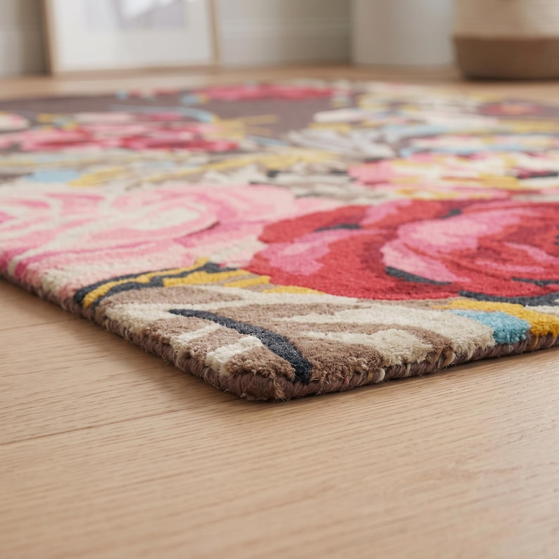 Low-angle close-up photograph of a hand-tufted wool floral rug resting on a wooden floor, highlighting its pile height and edge construction.